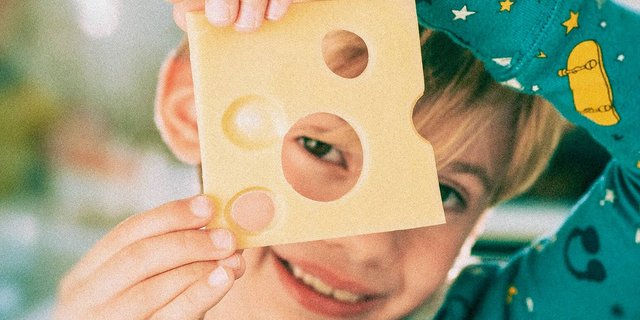 Knabe schaut durch das Loch in einer Scheibe Emmentaler Käse.