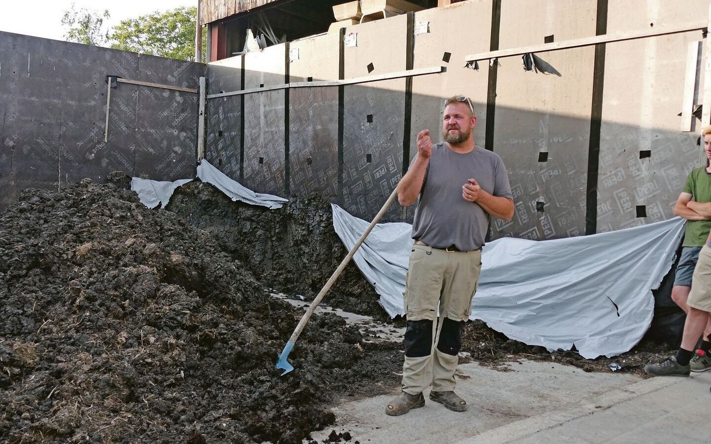 Anno Lutke Schipholt zeigt den Teilnehmer(innen) den Hofmist, der nach dem Prozess der mikrobiellen Carbonisierung nach frischer Erde riecht.